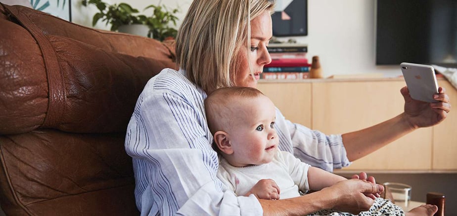 Mor med barneforsikring fra Frende, baby på fanget og tar legetime på mobilen.