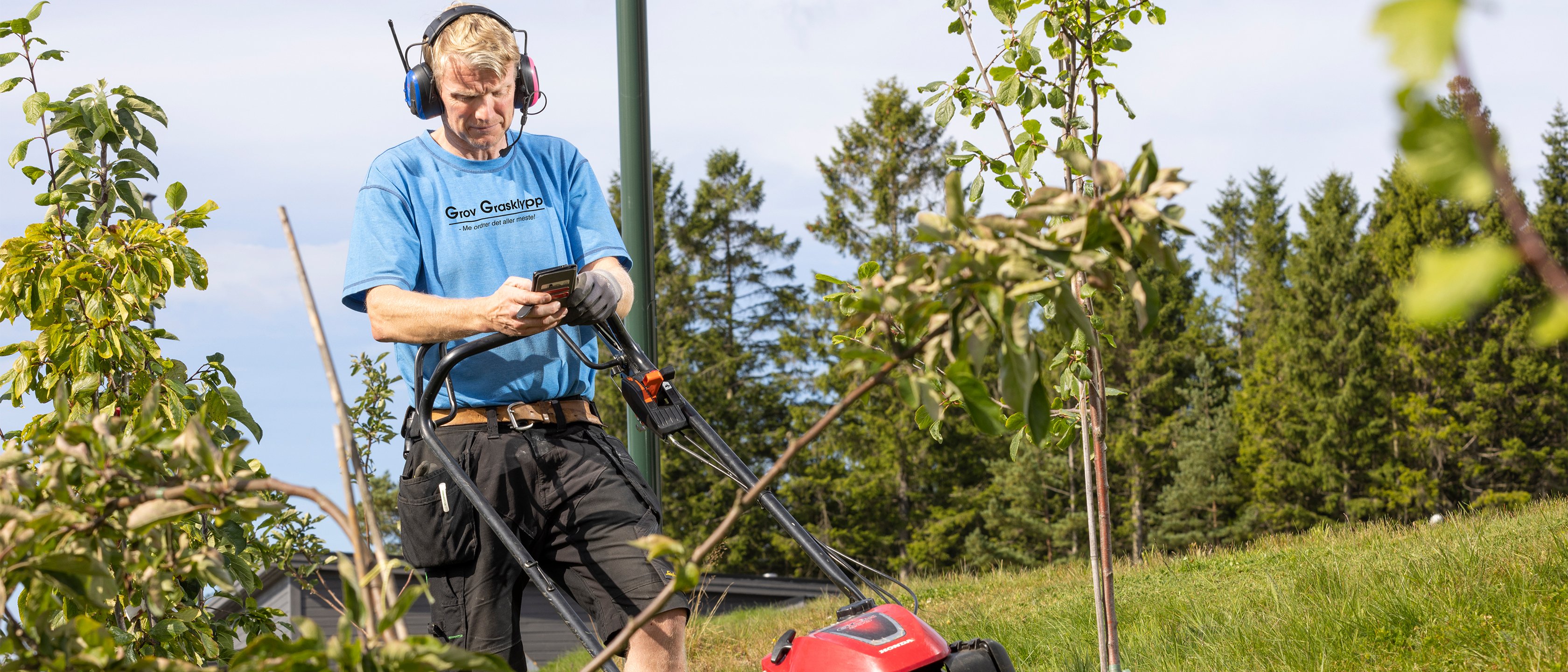 mann klipper gresset mens han ser på mobilen