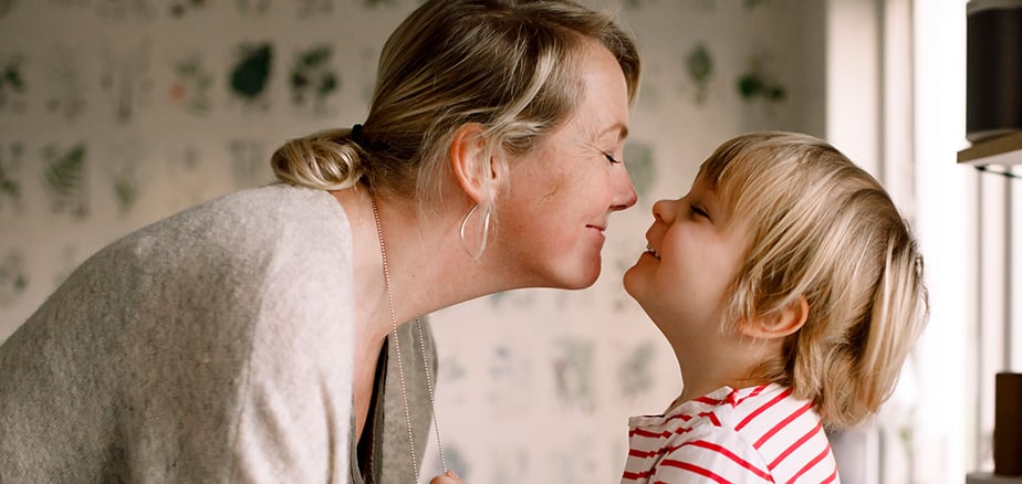 Mor og barn smilende med ansiktet tett inntil hverandre.