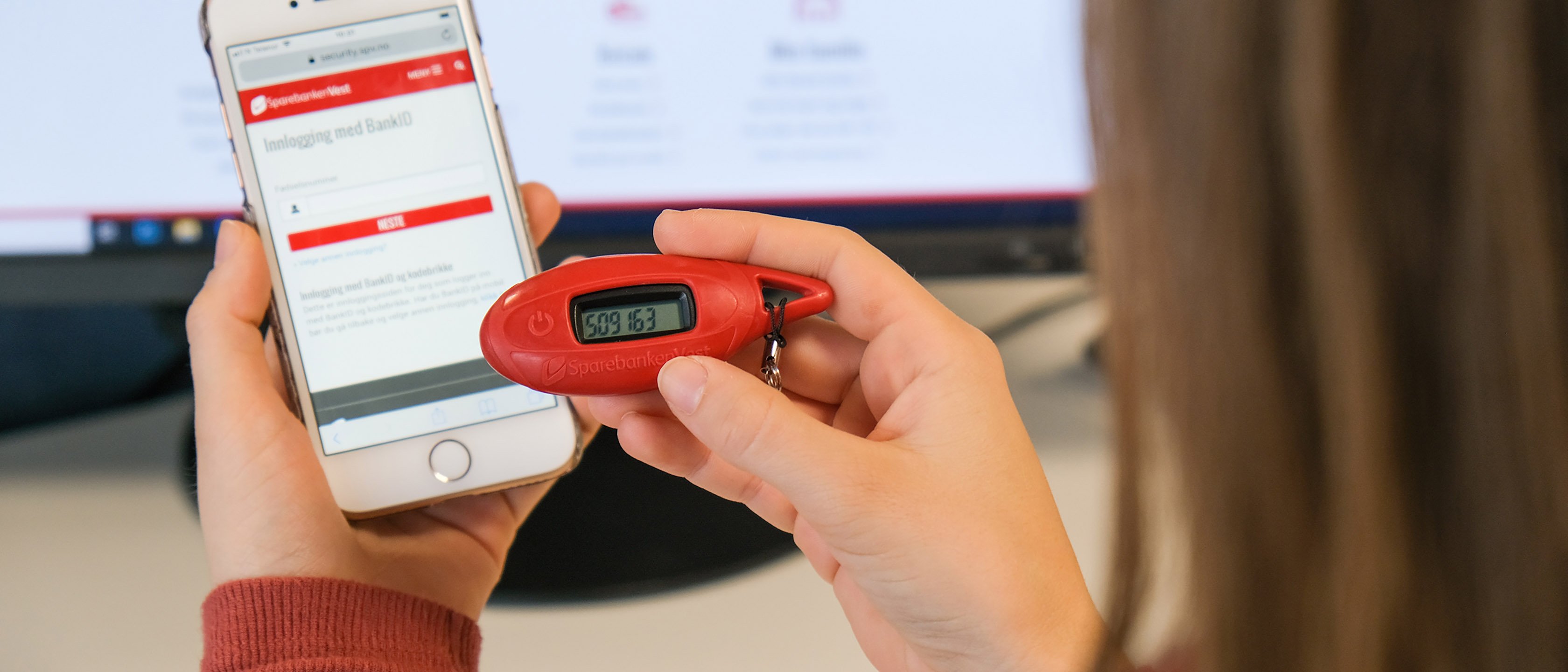 Dame som holder en iPhone og kodebrikke fra Sparebenken Vest foran seg. Innlogging med bankID vises på skjermen.