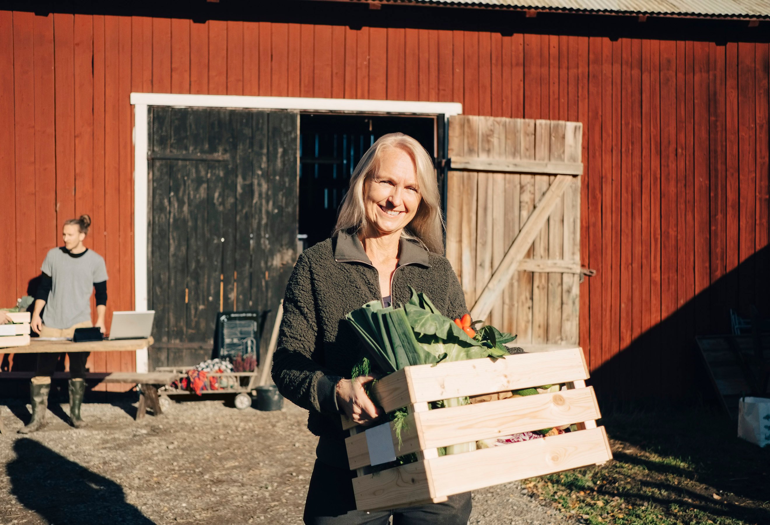 Dame på bondegård holder kasse med grønnsaker.