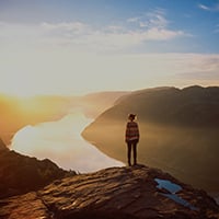 Kvinne står og ser utover fjorden i solnedgang