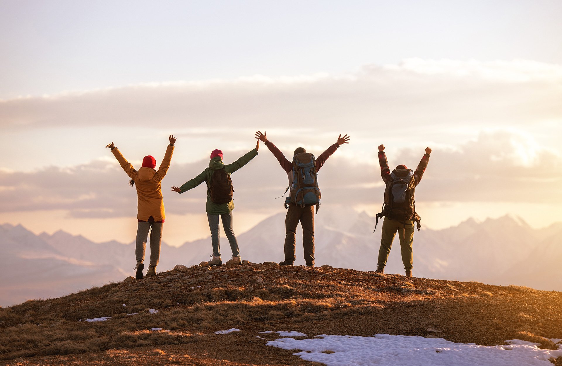 Fire personer står på toppen av et fjell og strekker armene i været. 