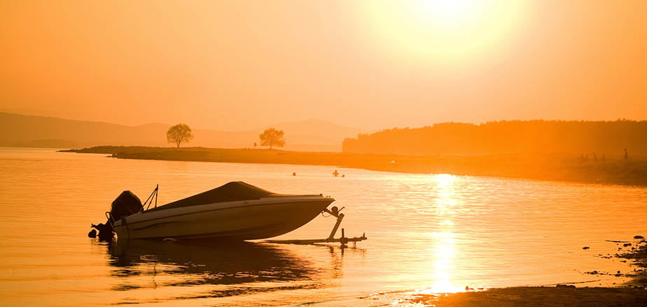 Båt som ligger forankret i fjæra med solnedgang i bakgrunnen