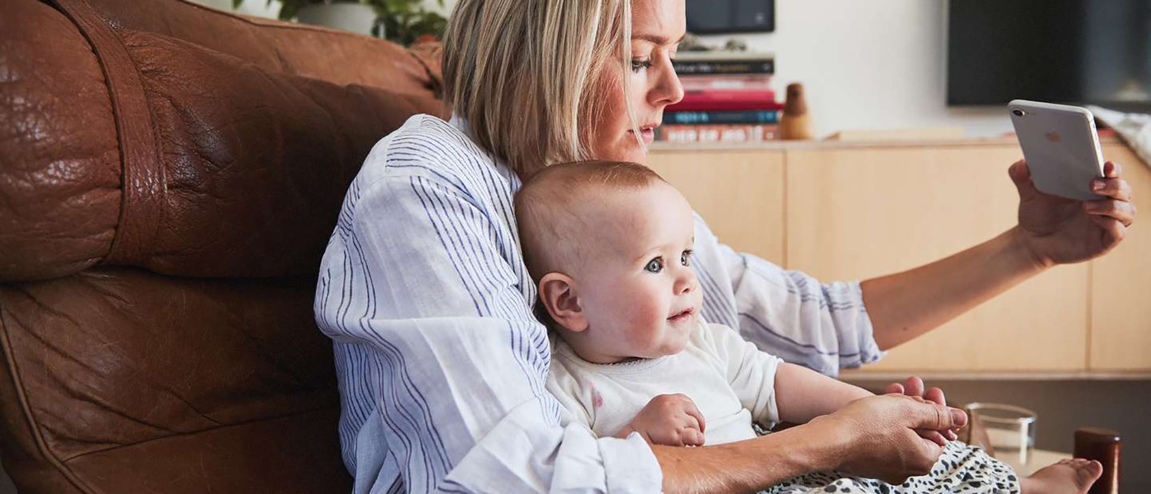 Mor med barneforsikring fra Frende, baby på fanget og tar legetime på mobilen.