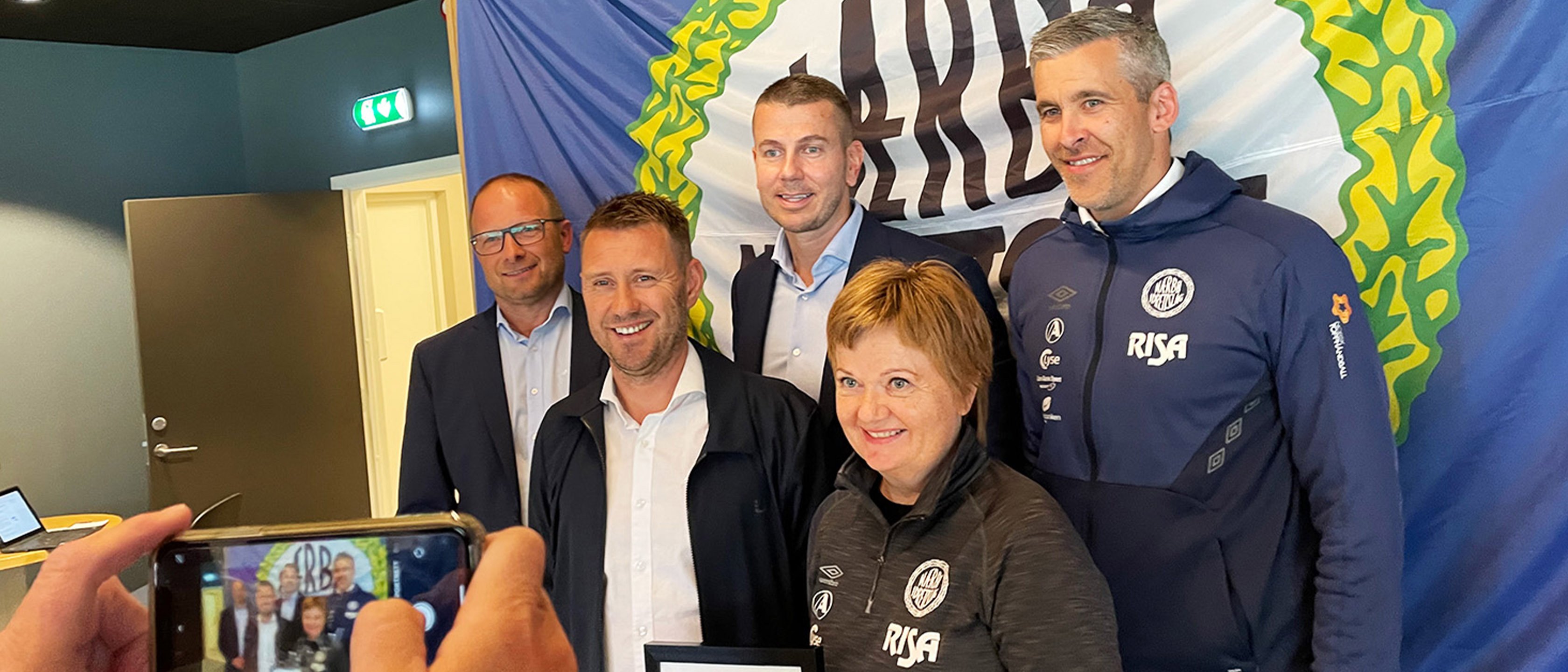 Representanter fra Nærbø IL og regionsdirektør Simen Aarskog foran Nærbø-logo. 