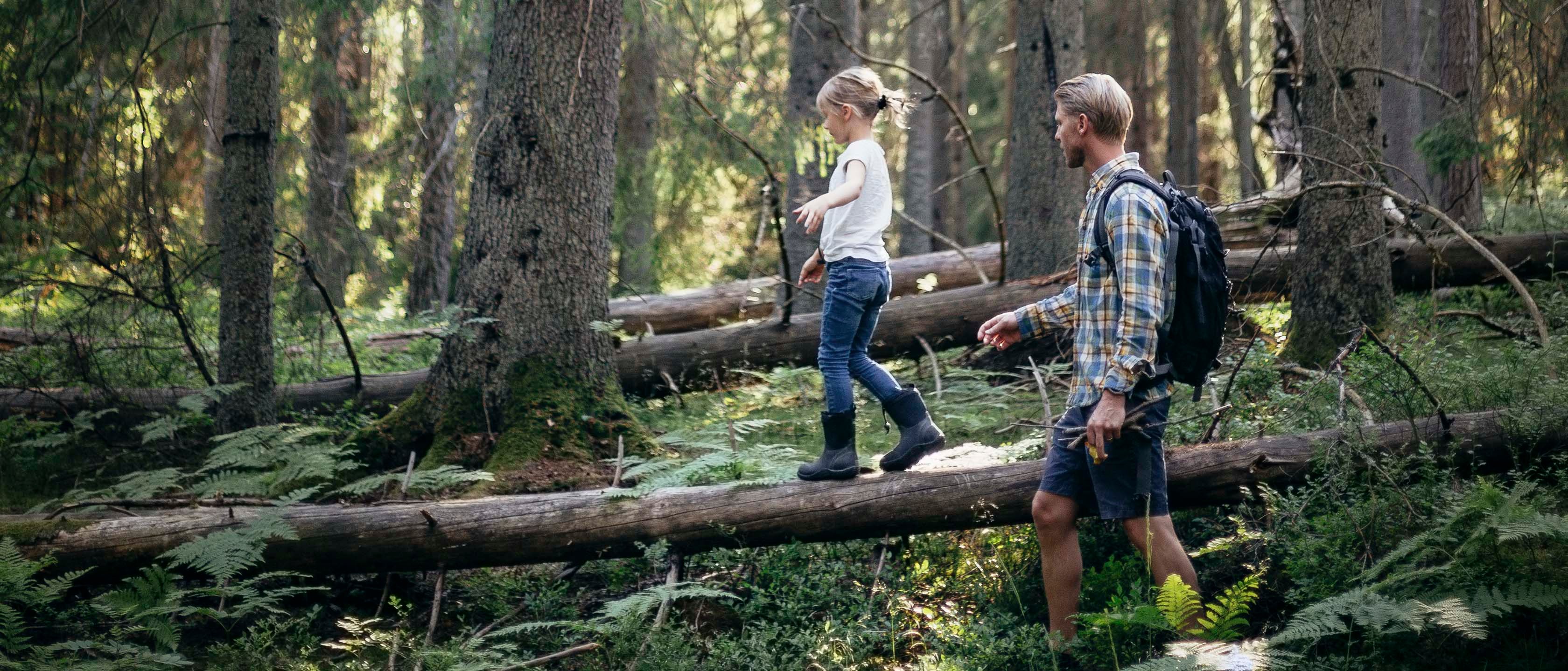 Far og datter balanserer på felte trær i skogen.