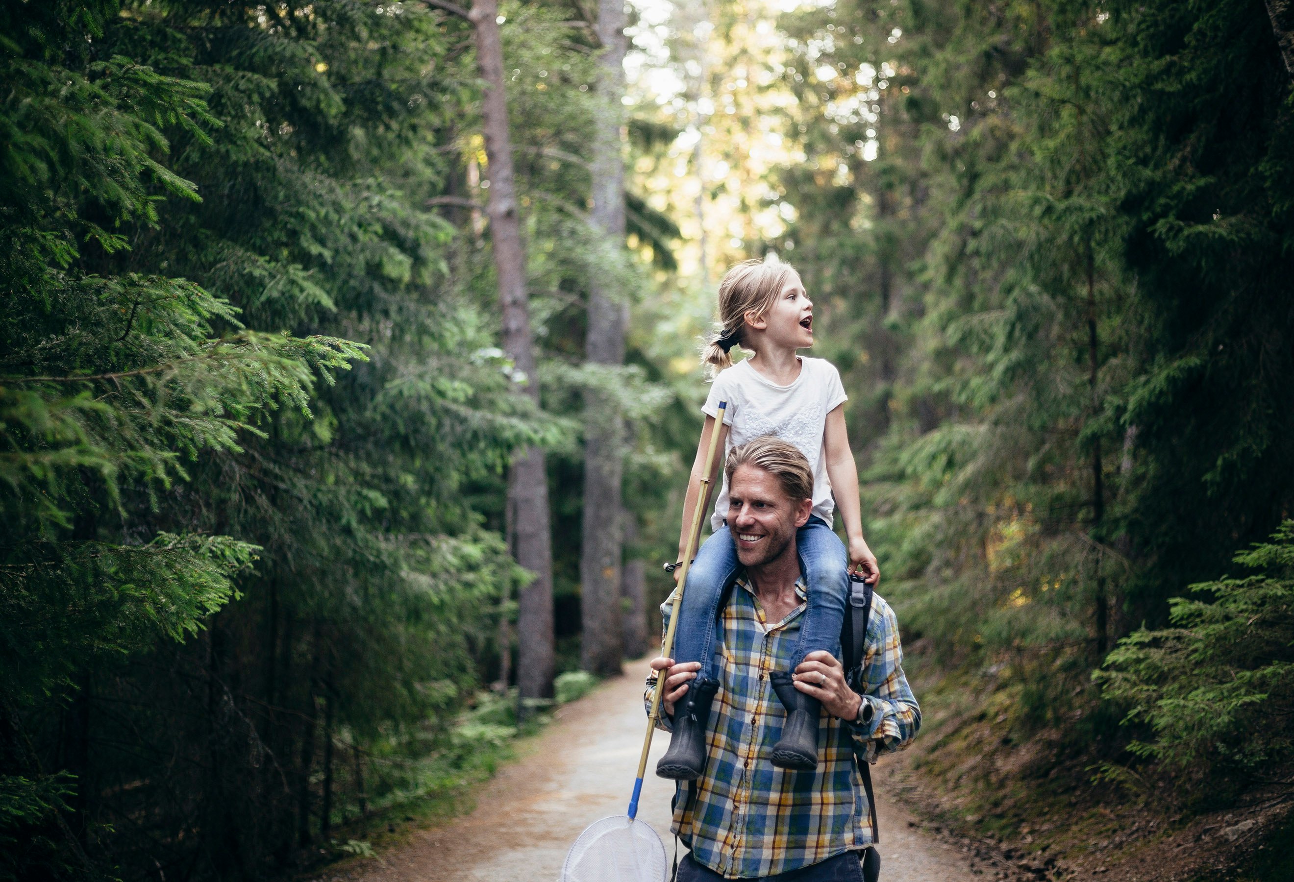 Mann med jente på skuldrene på tur i skogen.