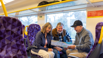 Three friends on a V Line train looking at a map and smiling