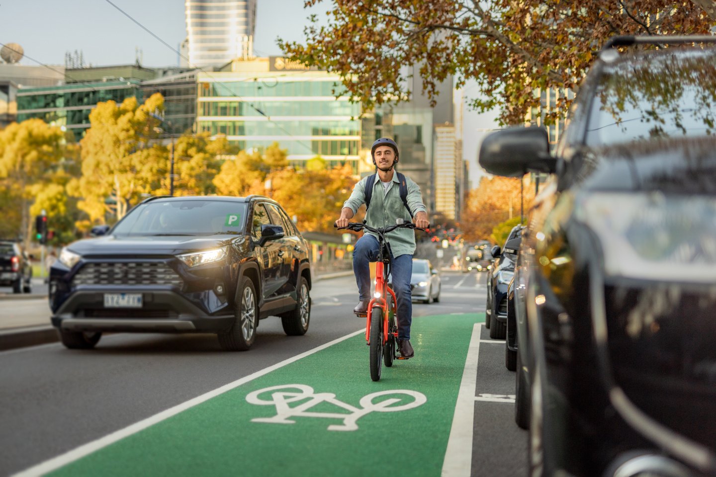 A man pedals his bike along a bright green bike lane surrounded by trees and grass.