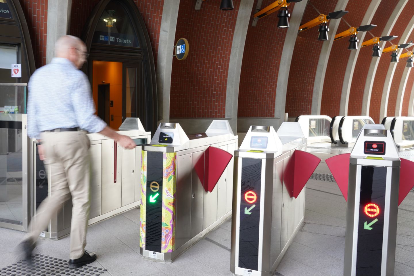 A man walks through a wide myki gate at Arden station. He is tapping a card on the gate reader.
