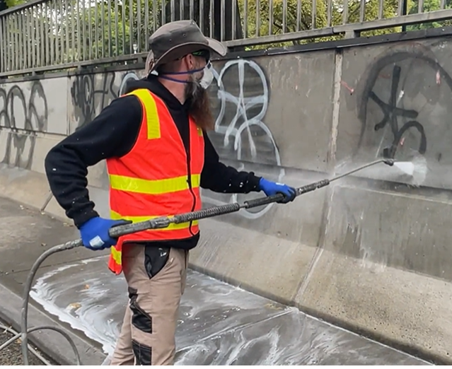 Image of worker dressed in high vis removing graffiti using a high pressure water gun