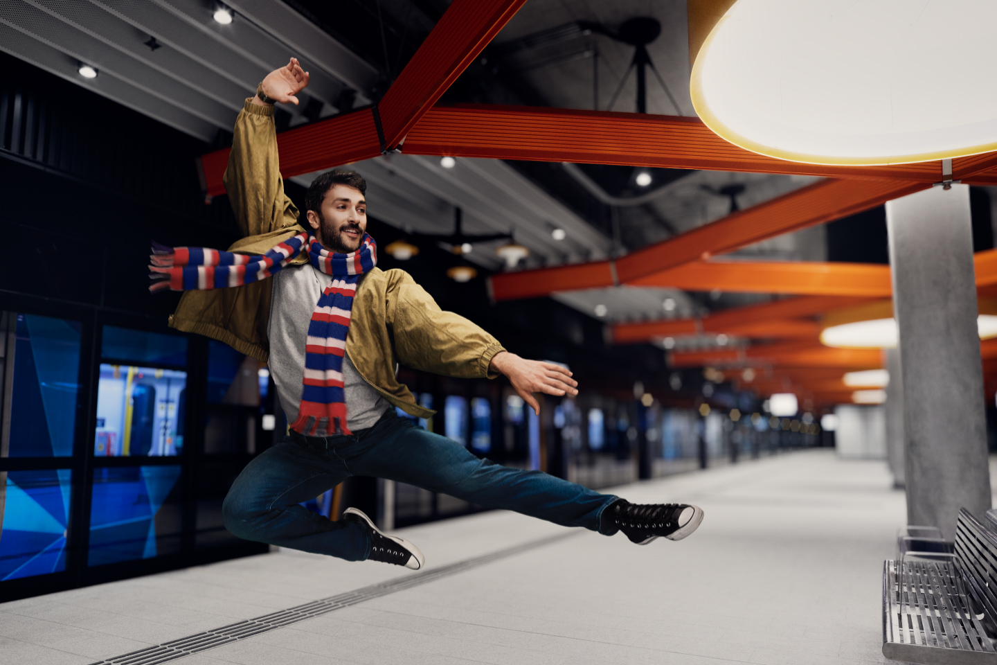 Image of a man wearing a red, white and blue striped scarf and jumping with legs and arms extended