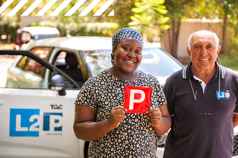 Image of woman holding a red P plate standing next to an L2P Mentor driver.