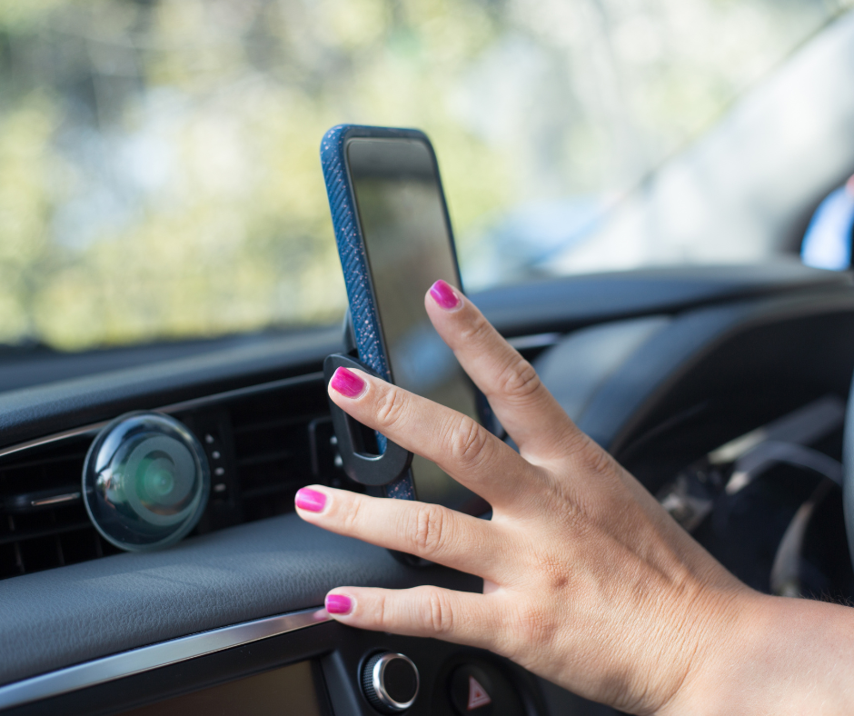 Image of a mobile phone mounted on a car dashboard with a hand on the screen