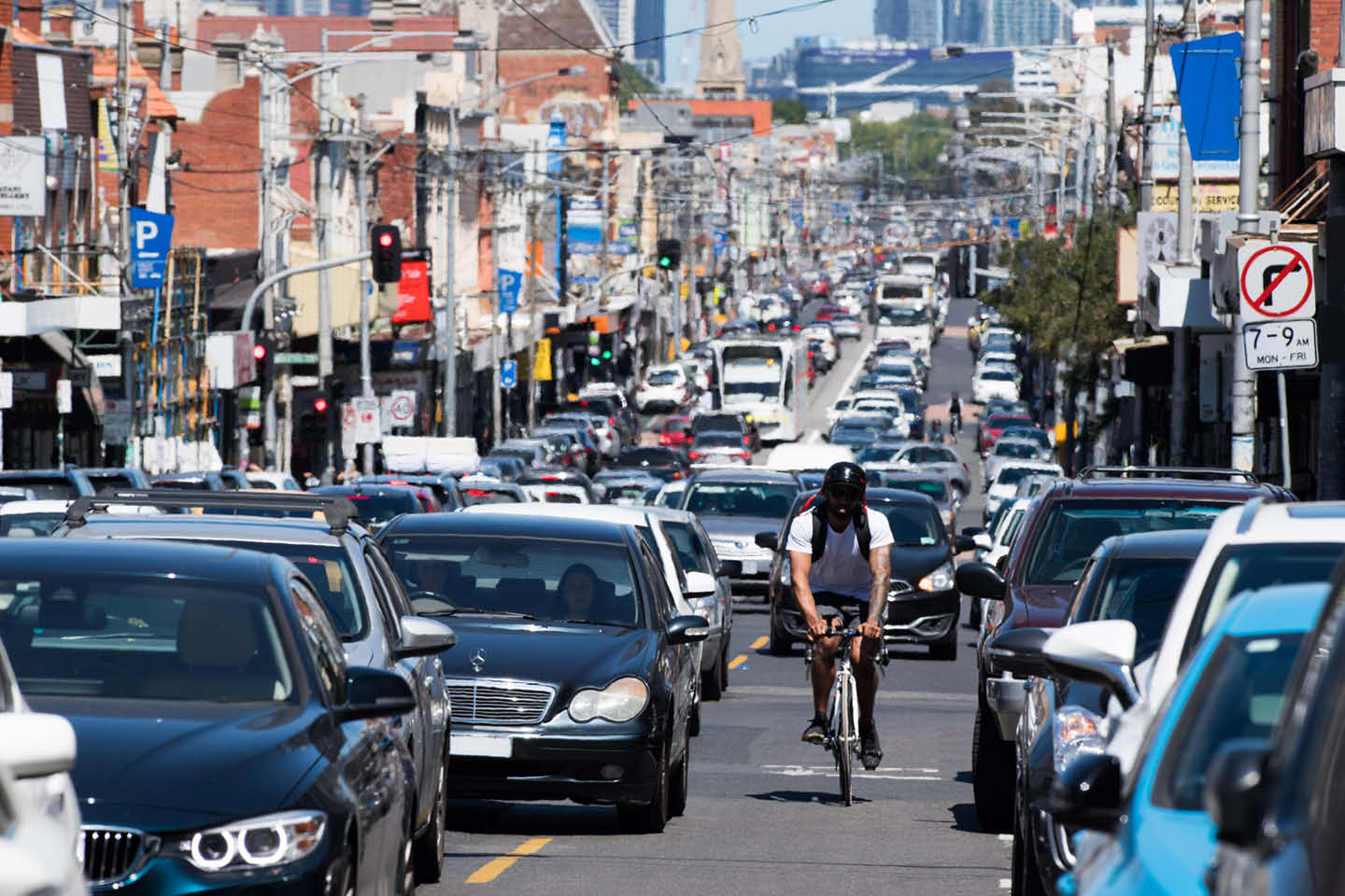 Photograph looking down a main road with cars and a cyclist during peak hour traffic