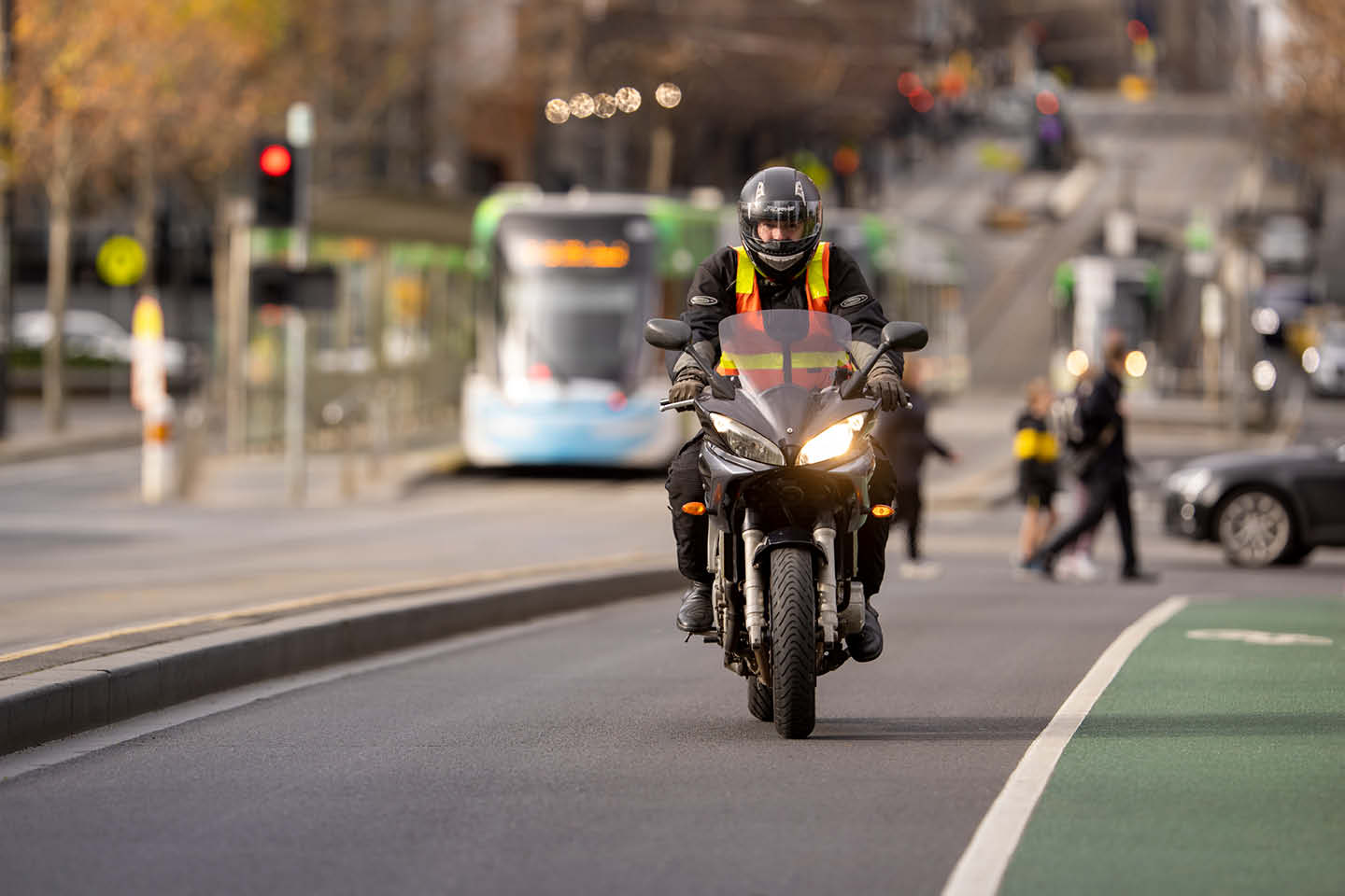 Photograph of a man on a motorbike wearing a high-vis vest, riding through the CBD