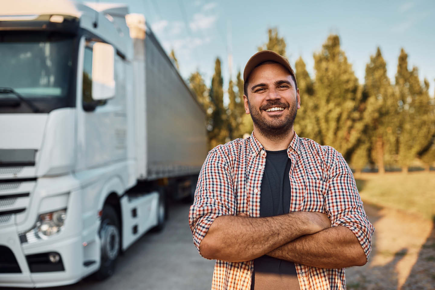 Photograph of a young man with arms crossed, smiling at the camera, while standing next to a commercial truck