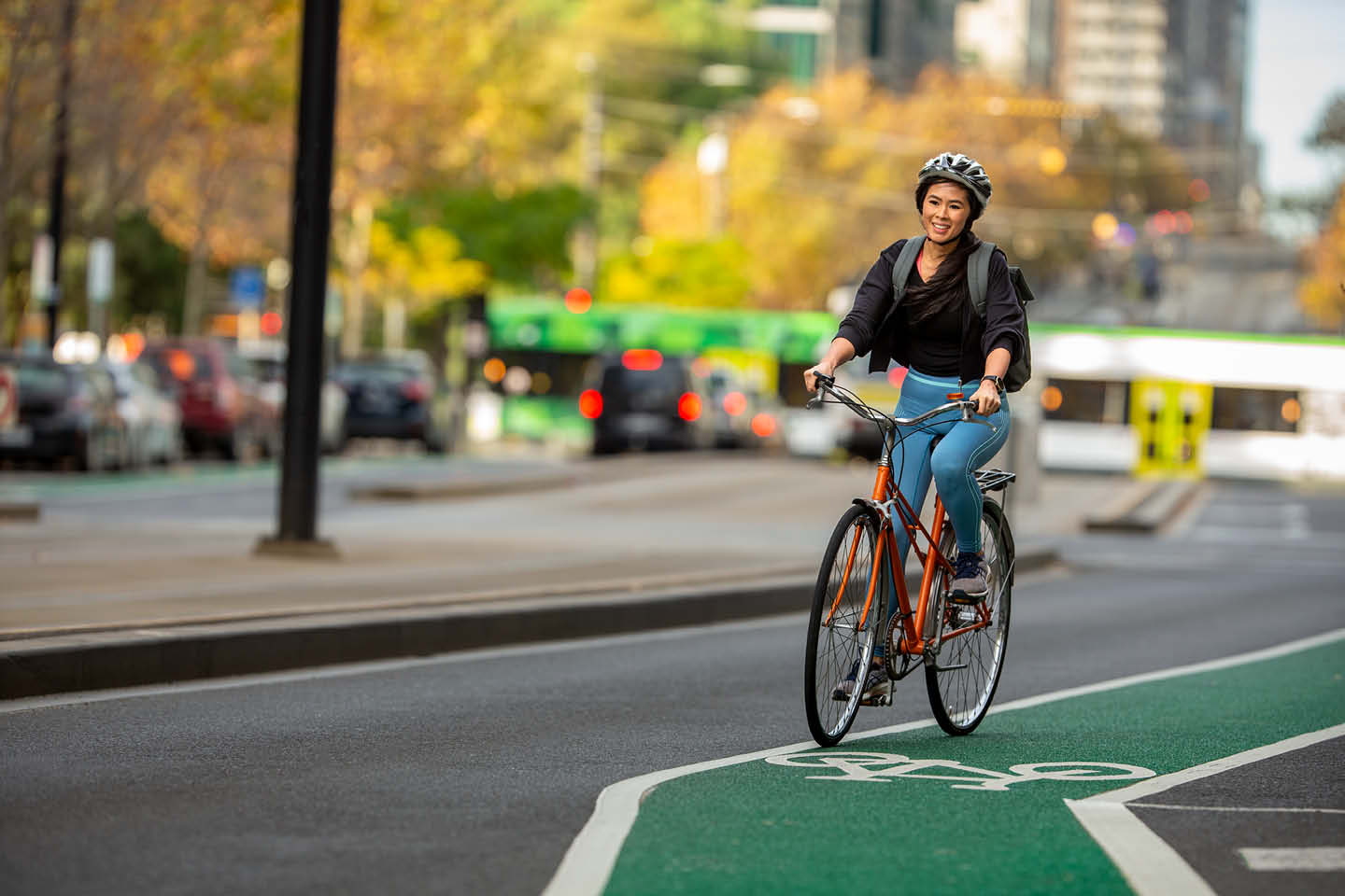 Photograph of a young woman on a bike, cycling along a bike lane