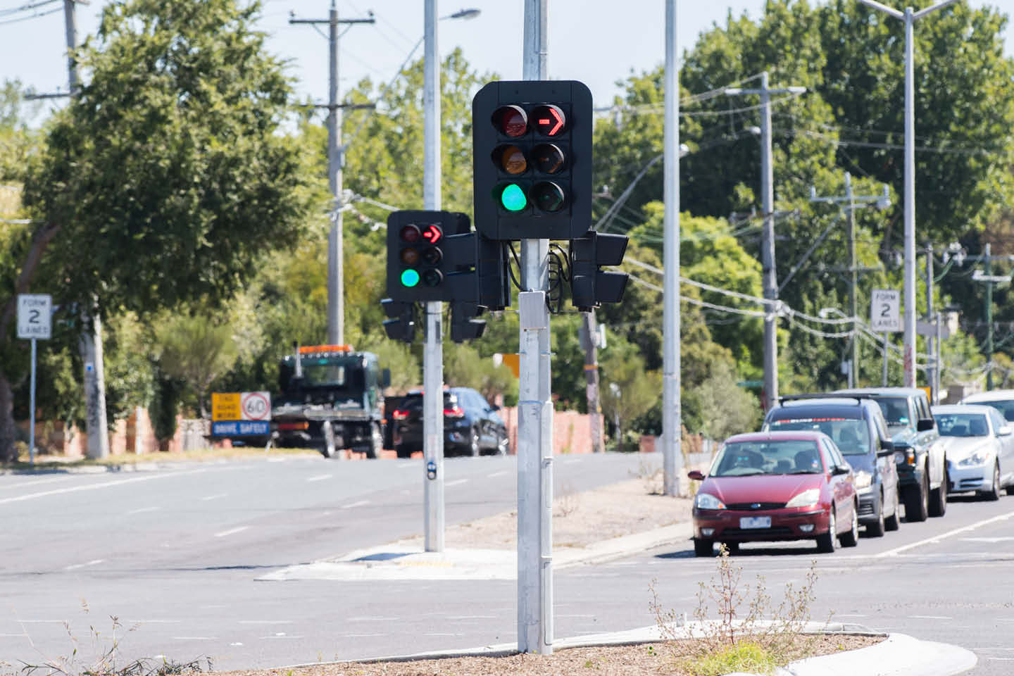 Photograph of an intersection with lights illuminated green, and a row of cars stopped on the opposite side