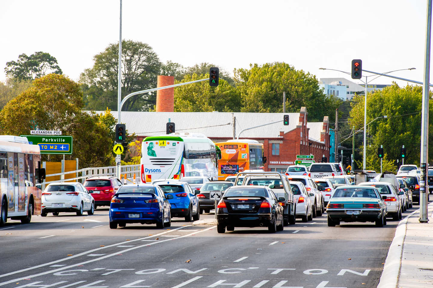 Photograph of four lanes of traffic with text and line road markings, focusing on the rear view of cars