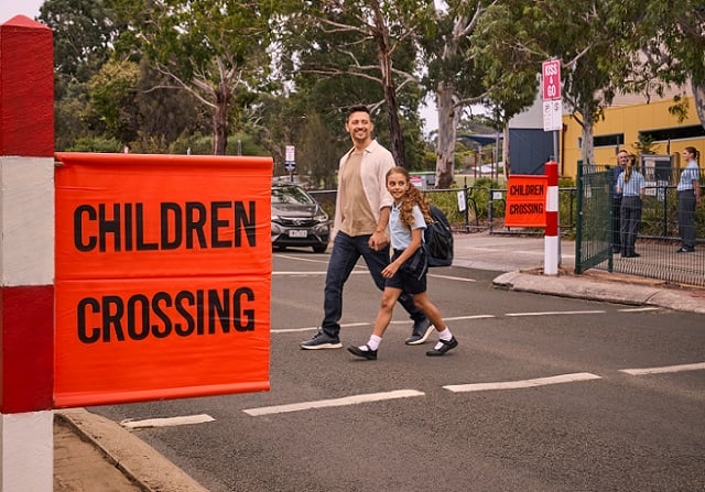 Image of a man holding a school students hand crossing at a children crossing