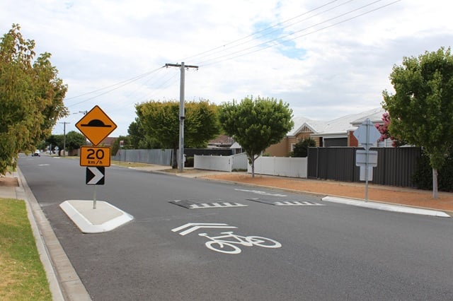 Image of cycling marking on a road next to a speed hump. 20 km/h yellow and black sign also shown on the speed hump.