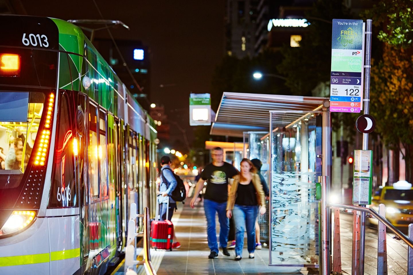 A city tram stop at night. There are passengers getting on a off the tram.