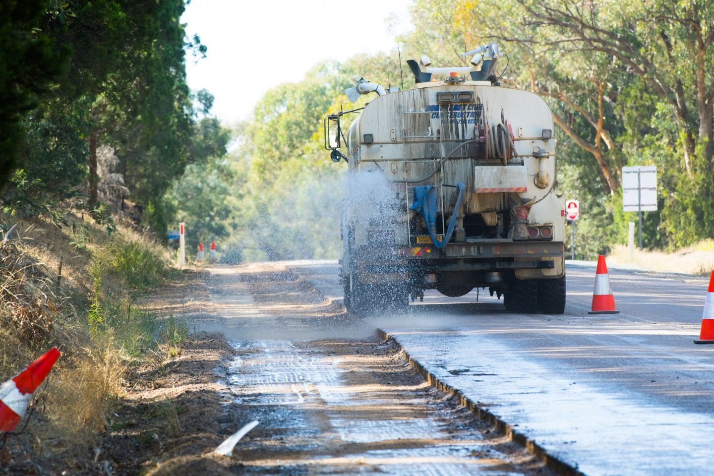 Roadwords truck spraying water on a section of road that's been dug up and is being resurfaced.