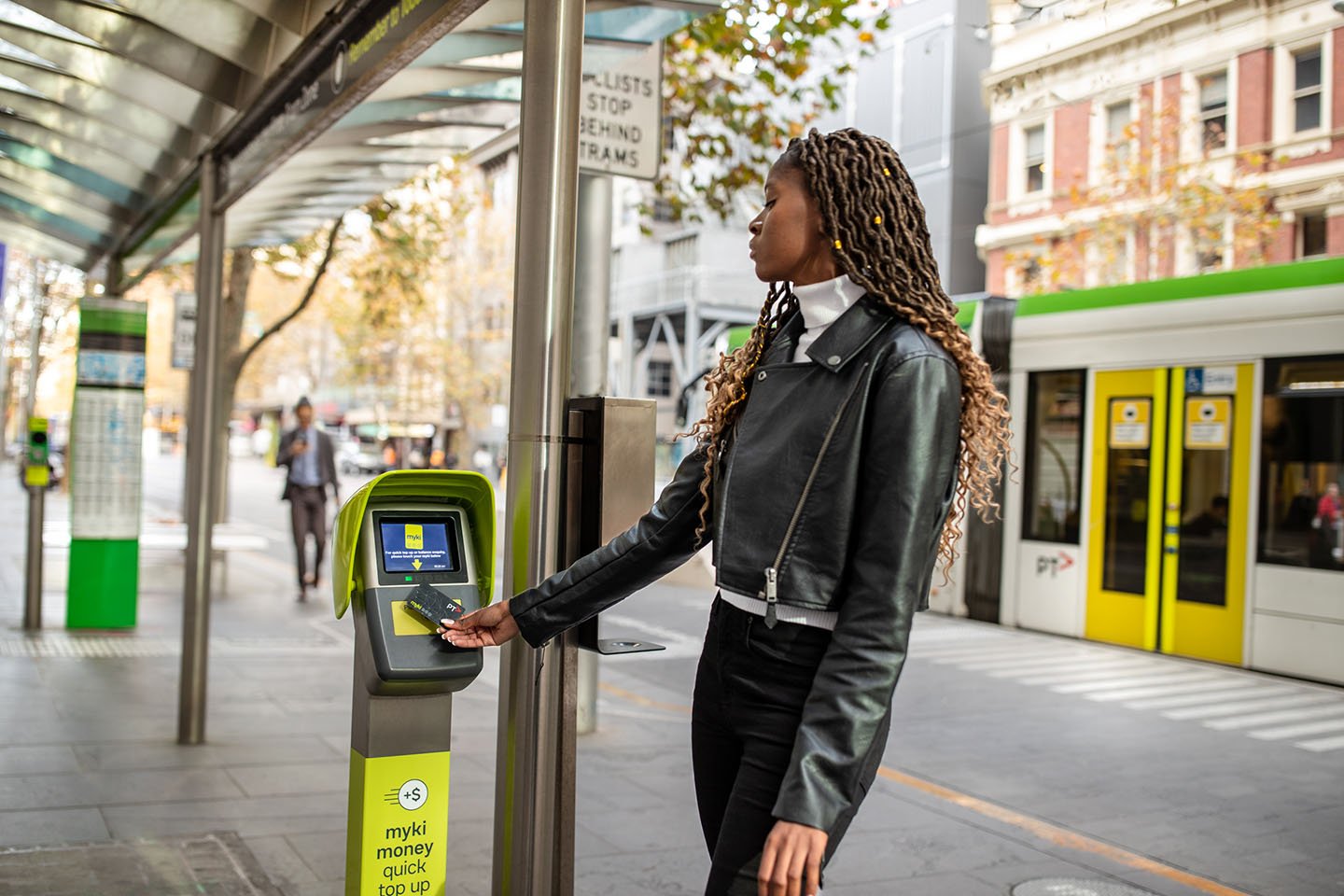 A woman using a myki top unit at a tram stop