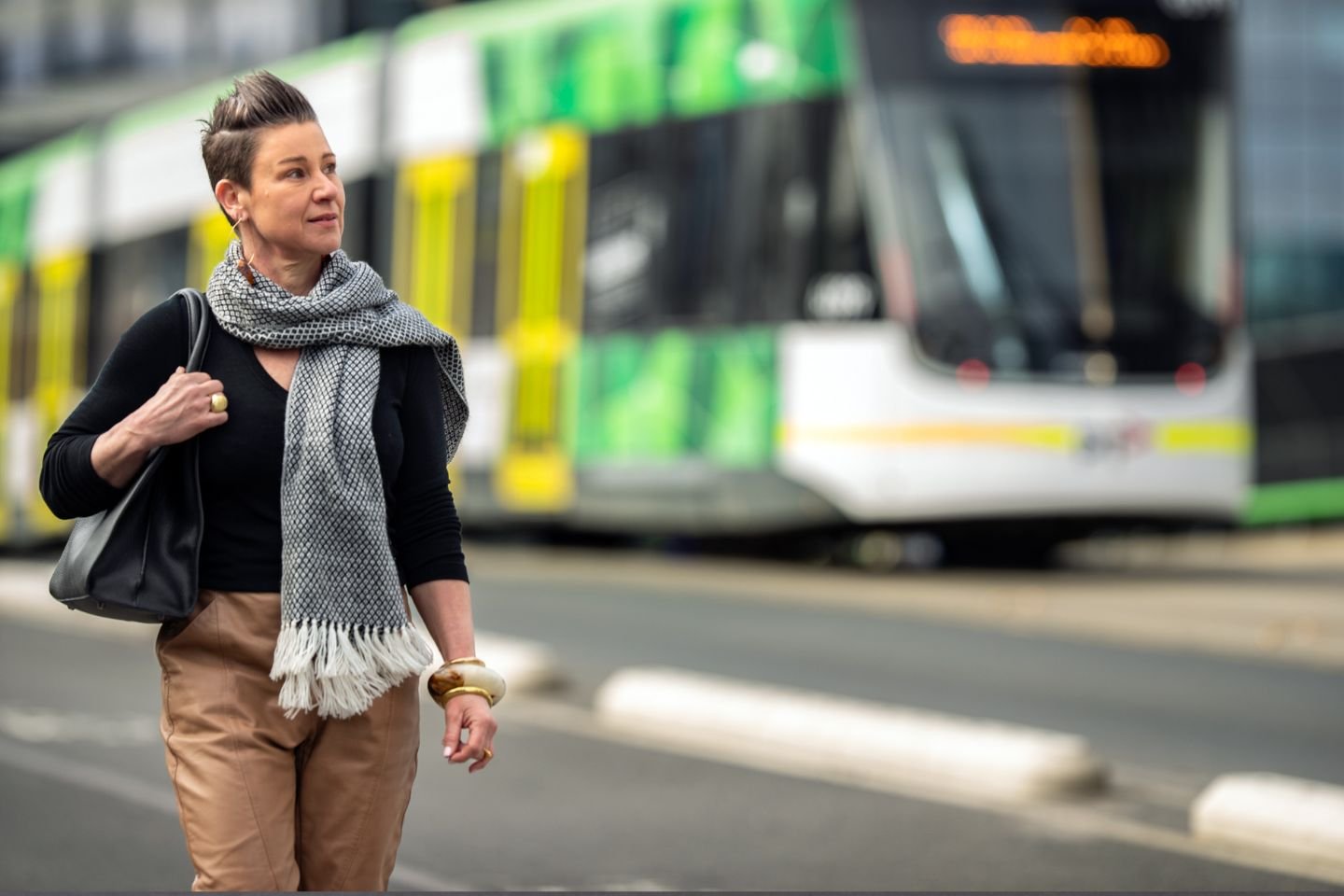 A woman walking along with a tram in the background.