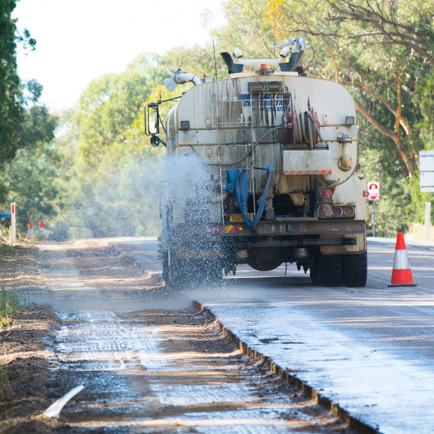 Roadwords truck spraying water on a section of road that's been dug up and is being resurfaced.
