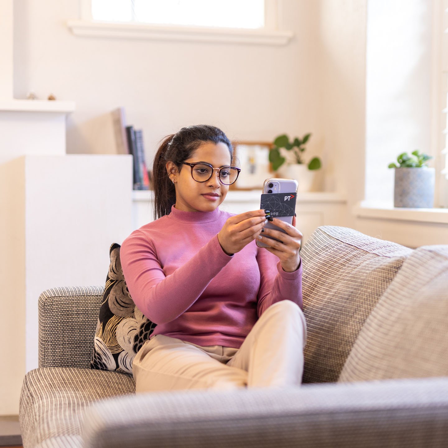 A woman sitting on a couch using her mobile phone. She also has her myki.