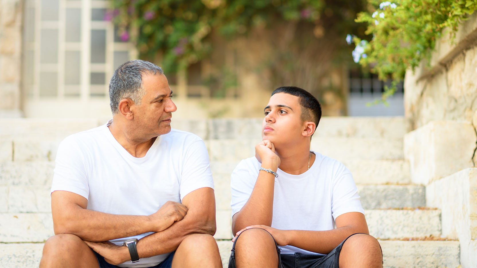 Father and teenage son have a conversation while sitting on steps outdoors.
