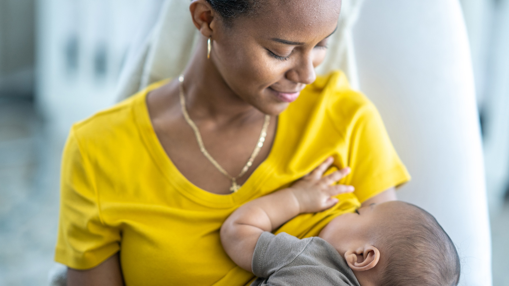 New mother sits in rocking chair as she breastfeeds her son