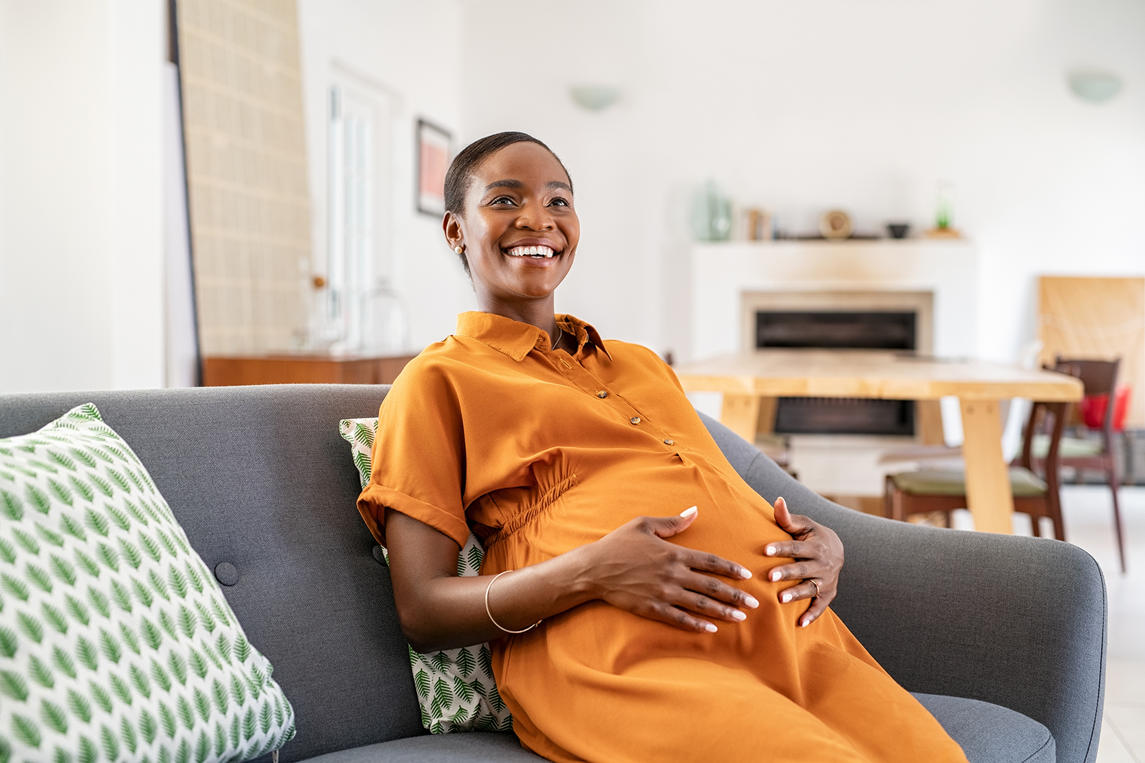 A smiling pregnant woman seated on a couch