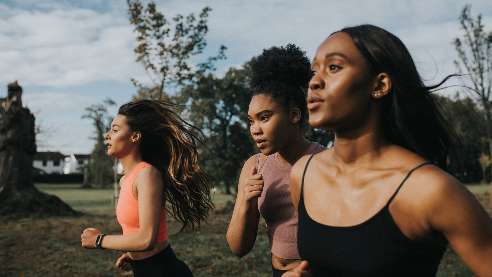 Strong, fit woman joggers, running through a sunny park at sunrise. They look determined as they put in the effort. Their hair blows behind them as they look in front of them.
