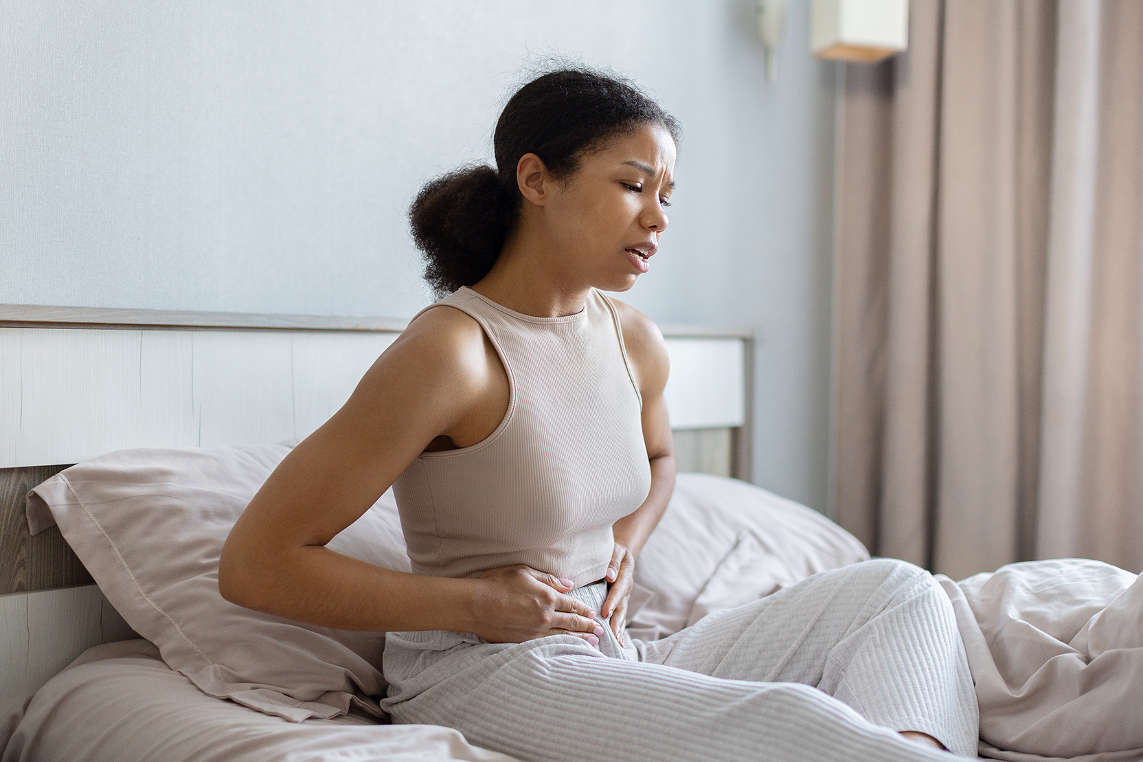 Woman holding stomach while sitting upright in bed