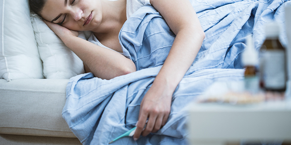 Woman sick in bed holding a thermometer