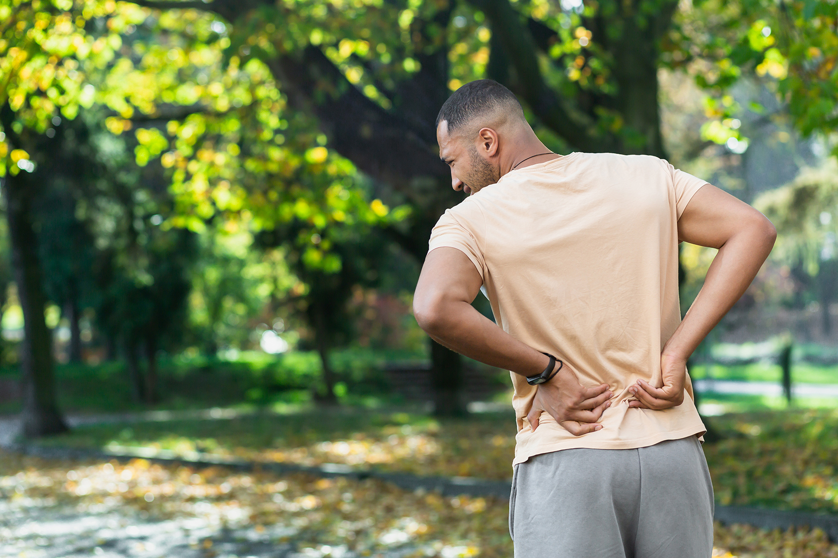 A man walking in a park presses his hands into his lower back due to hip pain 
