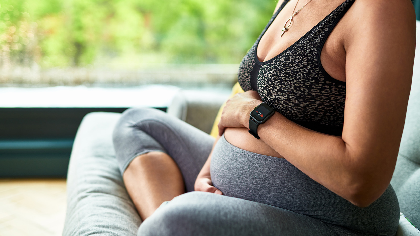 Heavily pregnant woman wearing fitness tracker holding bump