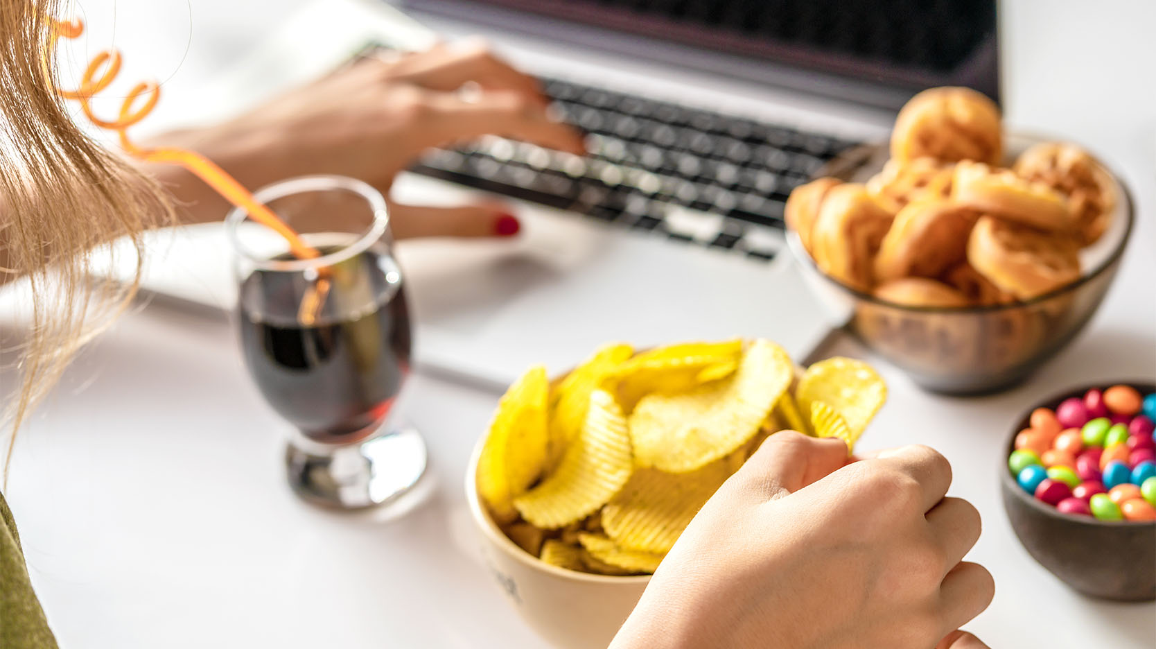 A person snacking on chips, cookies and candy while working on a laptop.