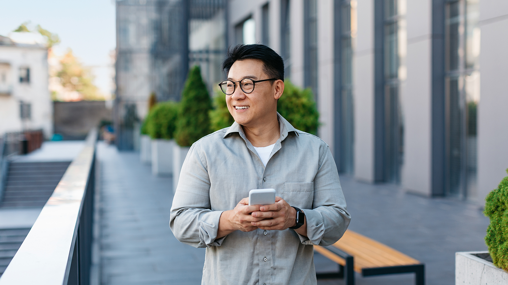 Middle-aged man checks messages on his smartphone while walking through a city.
