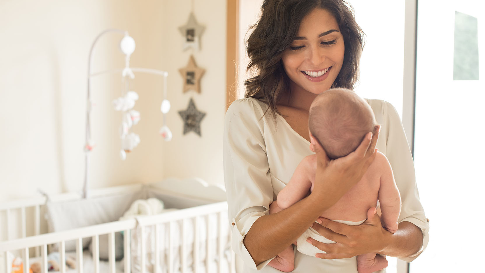 New mom smiles at her newborn son while holding him in a baby nursery.