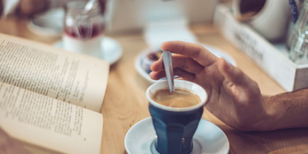 Close up of man about to pick up a cup of coffee from desk