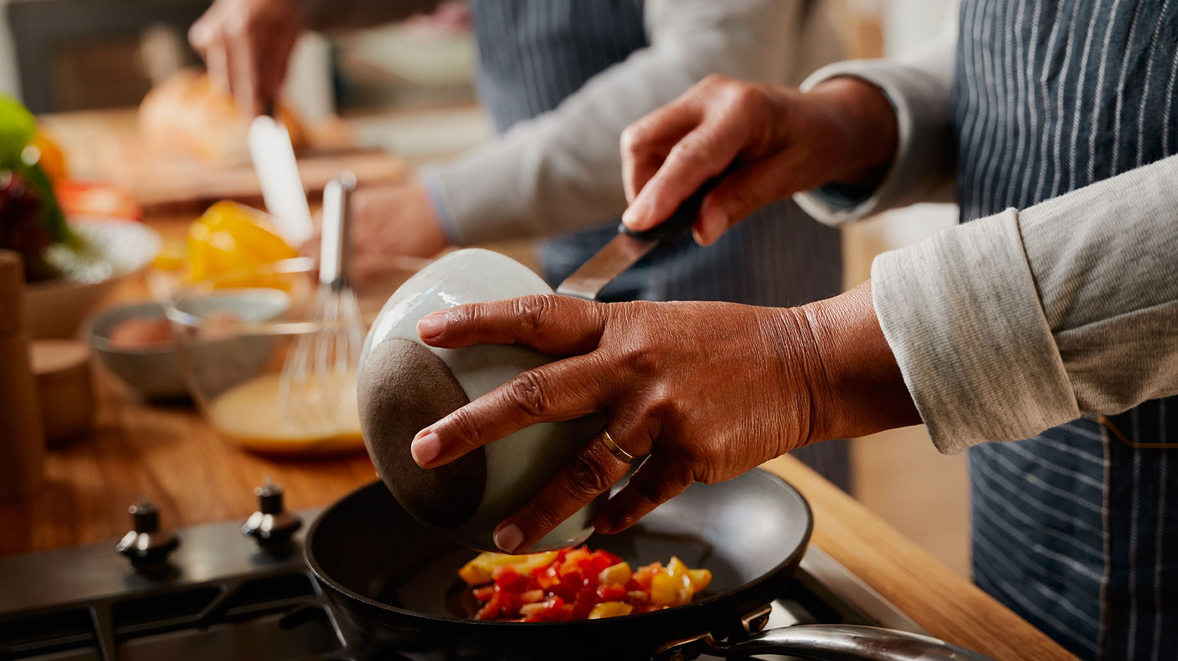 Hands of elderly couple cooking healthy breakfast together in kitchen at stove. 
