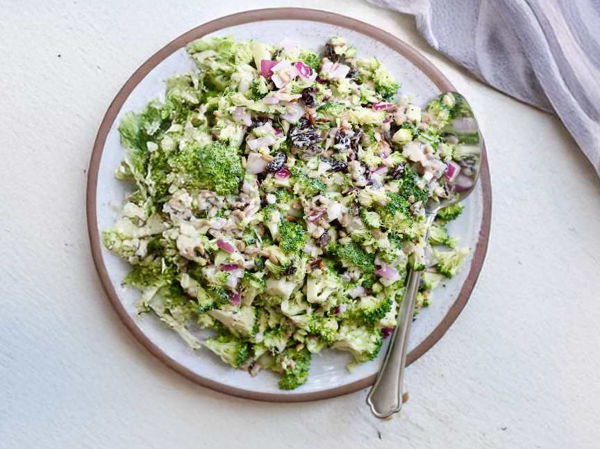 Broccoli salad on white plate with spoon on the side.
