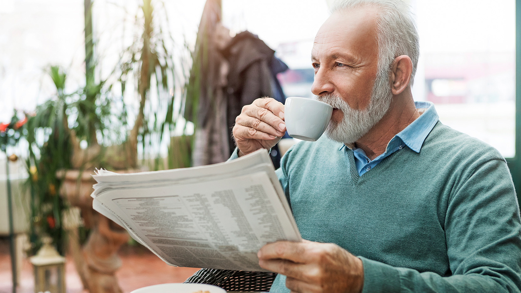 Senior man with newspaper drinking coffee.