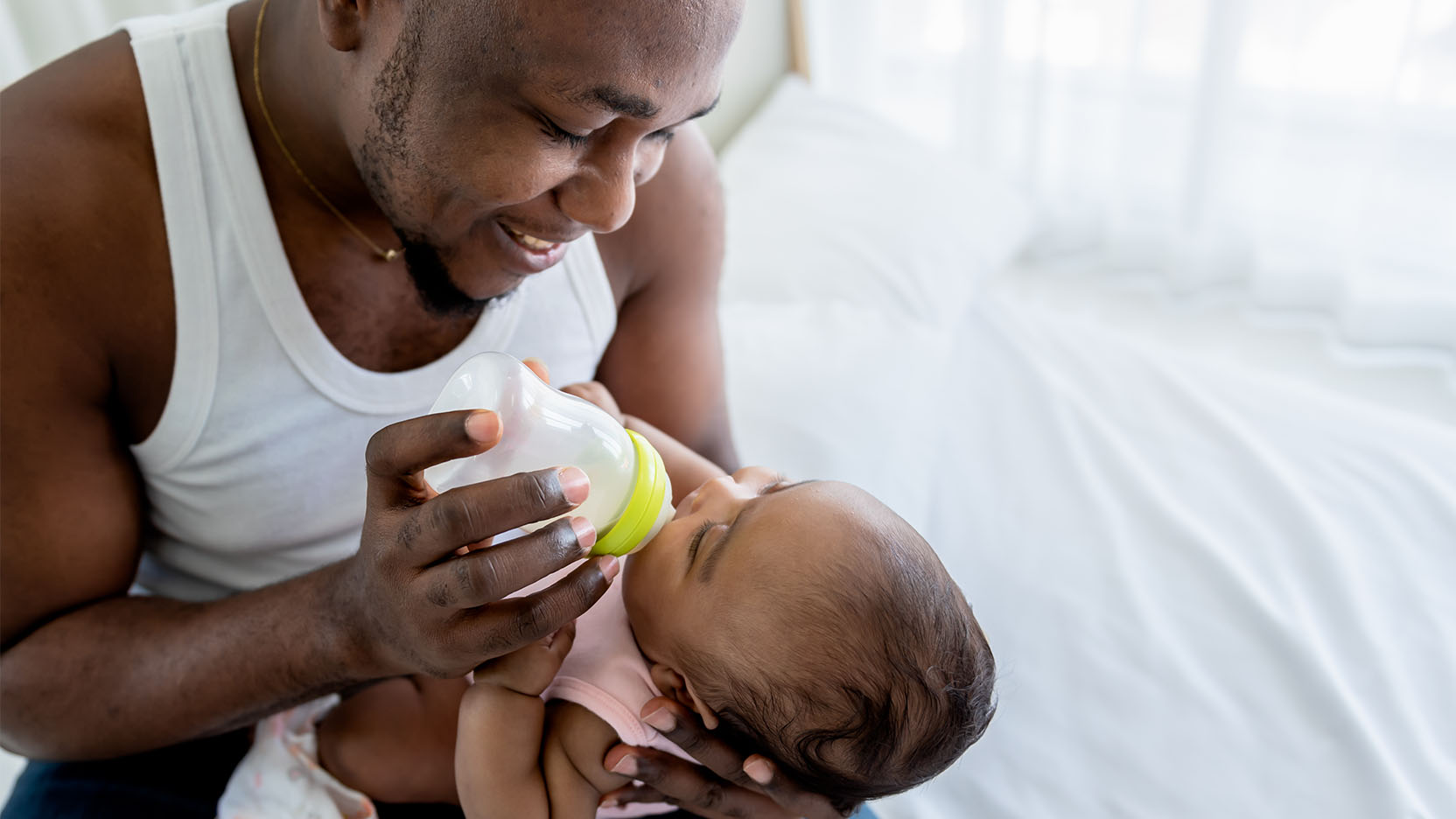Smiling father feeds his newborn baby a bottle.
