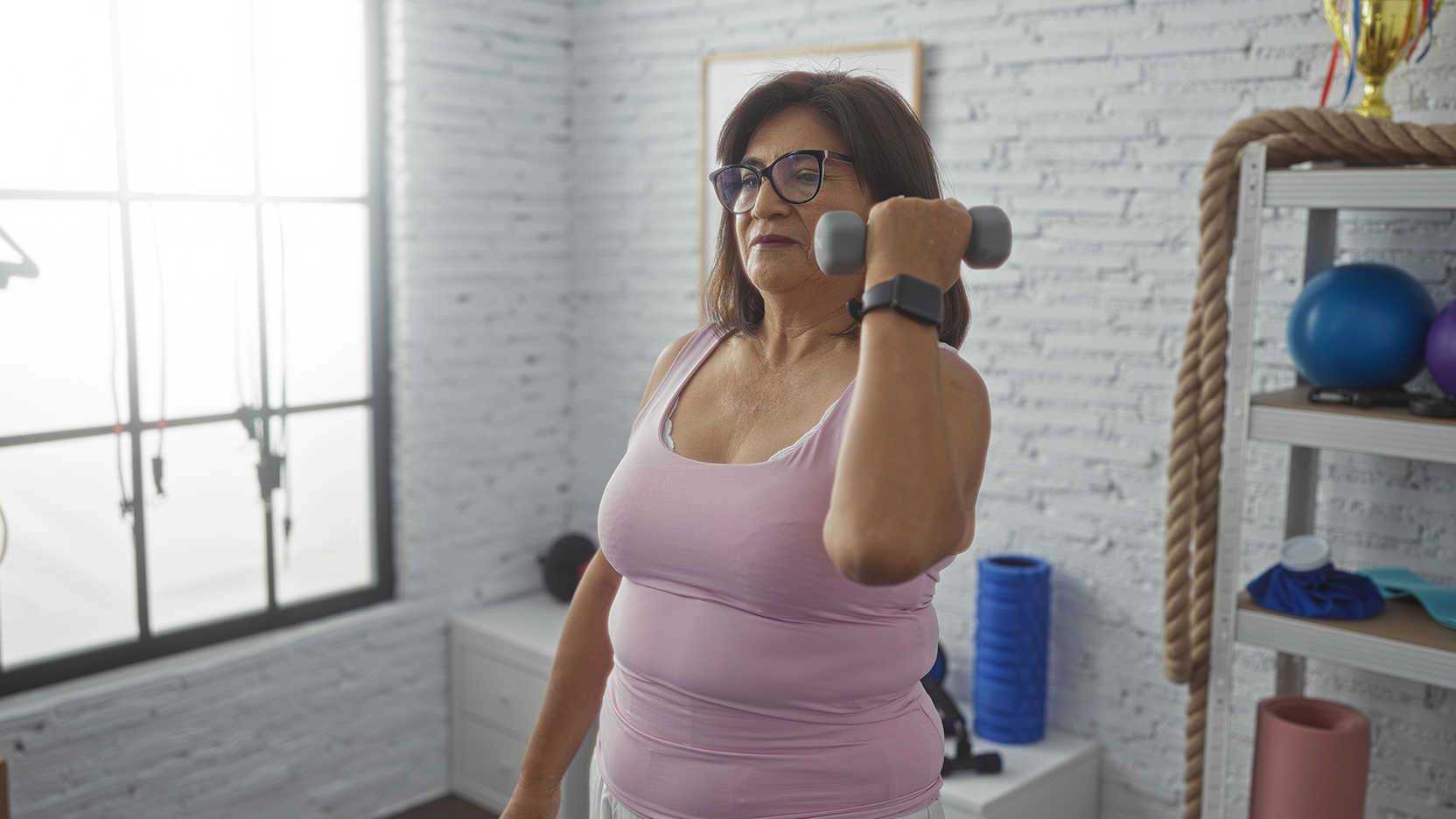 A middle aged woman lifts small weights during a cardiac rehabilitation session.